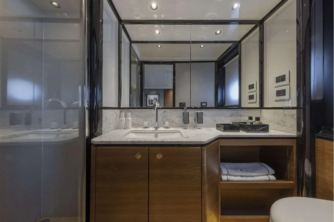 Modern bathroom featuring a marble sink with taps, wood cabinet, towels, mirrors, and controlled lighting. Clean and elegant design.
